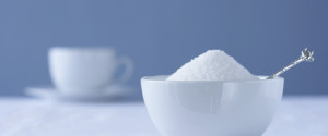Bowl of sugar on table, tea cup in background