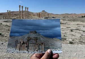 A general view taken on March 31, 2016 shows a photographer holding his picture of the Arc du Triomphe (Triumph's Arch) taken on March 14, 2014 in front of the remains of the historic monument after it was destroyed by Islamic State (IS) group jihadists in October 2015 in the ancient Syrian city of Palmyra. Syrian troops backed by Russian forces recaptured Palmyra on March 27, 2016, after a fierce offensive to rescue the city from jihadists who view the UNESCO-listed site's magnificent ruins as idolatrous. / AFP / JOSEPH EID (Photo credit should read JOSEPH EID/AFP/Getty Images)