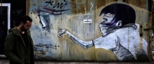 TOPSHOT - A man walks past a graffiti depicting a man throwing a petrol bomb on March 17, 2017 in the Greek capital, Athens. Greek authorities on March 17, 2017 were trying to determine how a near-defunct militant group was able to sneak at least two parcel bombs through airport security, one of which exploded at the IMF offices in Paris. The investigation so far suggests that the booby-trapped mail sent to the IMF and the German finance ministry -- presumably by a far-left group called the Conspiracy of Fire Nuclei -- failed to raise an alarm because it contained only a small amount of gunpowder. / AFP PHOTO / Angelos Tzortzinis (Photo credit should read ANGELOS TZORTZINIS/AFP/Getty Images)