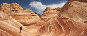 Adult male tourist hikes across the striated sandstone rock formations known as the Wave located within the Paria Canyon-Vermilion Cliffs Wilderness, Page, Arizona, US, North America
